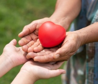 Manos de diferentes generaciones sosteniendo un corazón rojo, símbolo de solidaridad y apoyo de la Fundación Crecemos y Creemos